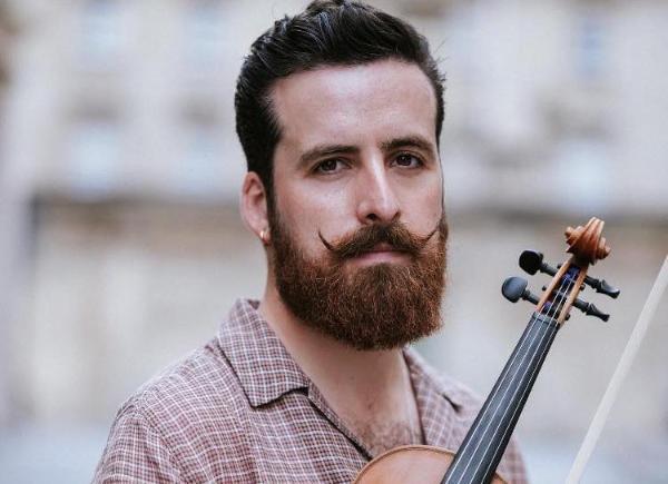 Nik Jovcic-Sas poses with his violin. They have a beard and a stylish moustache with upturned corners.