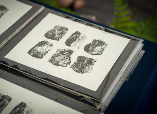 a black and white print of Stanton Drew stone circle in a black frame. Multiple are piled up on a table with greenery in background.