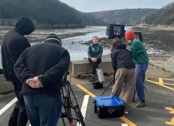 a film crew interviewing a lady sat in front of a beach